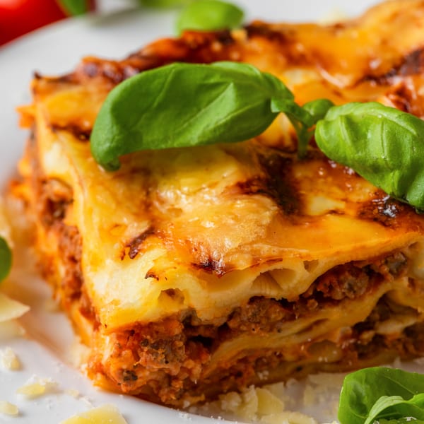 A close-up of a slice of lasagna with melted cheese, meat sauce, and fresh basil.