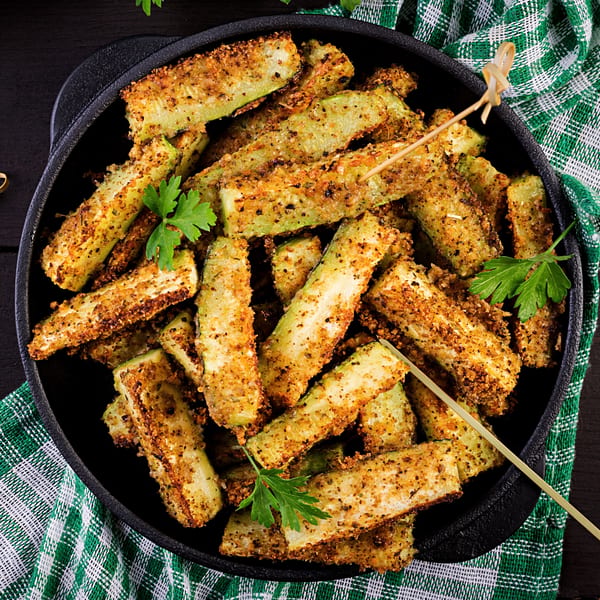 Crispy breaded zucchini fries in a black cast iron pan with a green and white checkered napkin.
