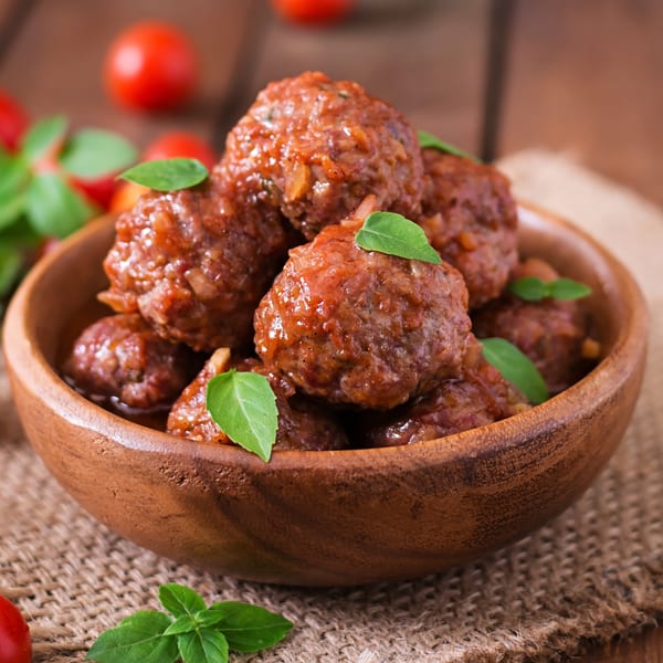 Fairway Pizza's meatballs in sauce with basil, served in a wooden bowl on a rustic surface.