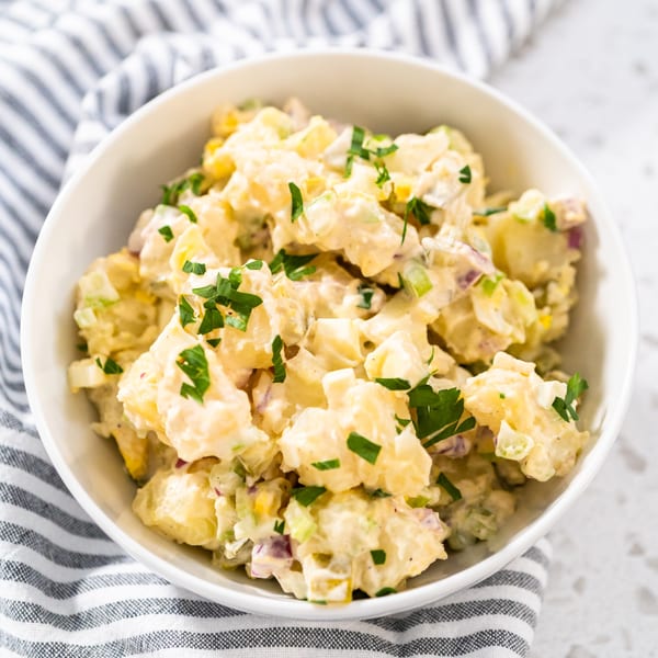 Creamy potato salad with chopped parsley, celery, and red onion in a white bowl.