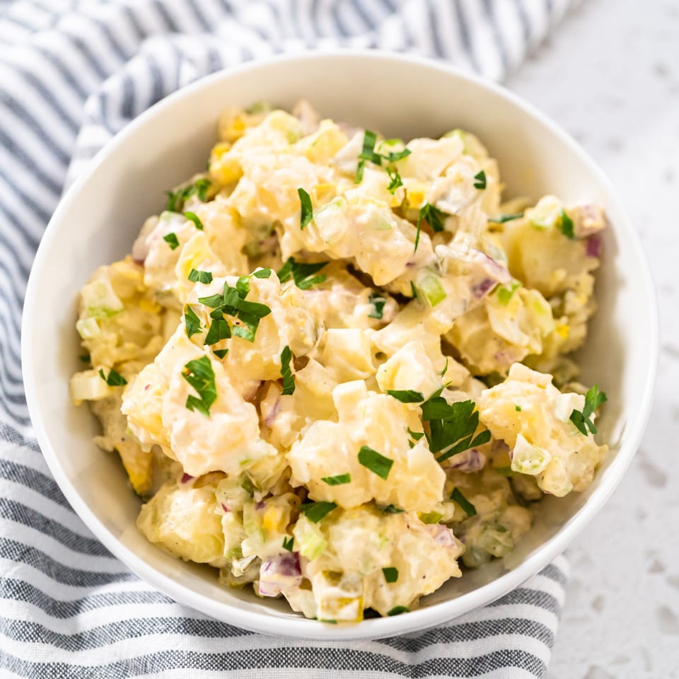 Creamy potato salad with chopped parsley, celery, and red onion in a white bowl.