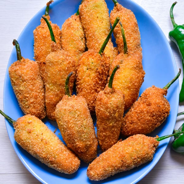 A blue plate filled with golden-brown, breaded jalapeño poppers, some with green stems visible.