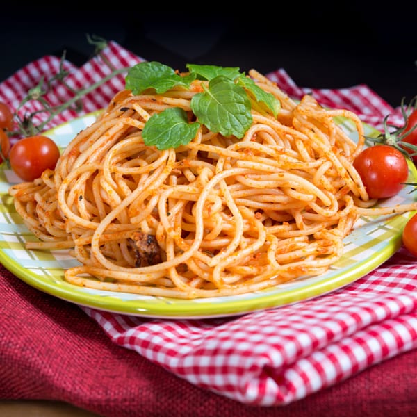 Spaghetti with red sauce and fresh mint on a checkered plate, surrounded by cherry tomatoes.