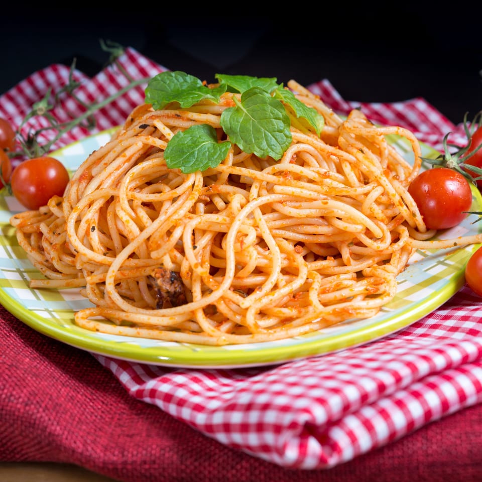 Spaghetti with red sauce and fresh mint on a checkered plate, surrounded by cherry tomatoes.