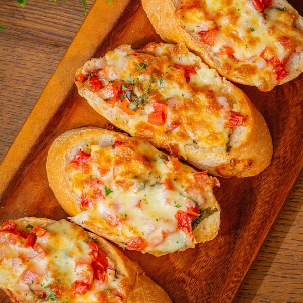Four cheesy Fairway Pizza bruschetta slices with diced tomatoes and herbs on a wooden board.
